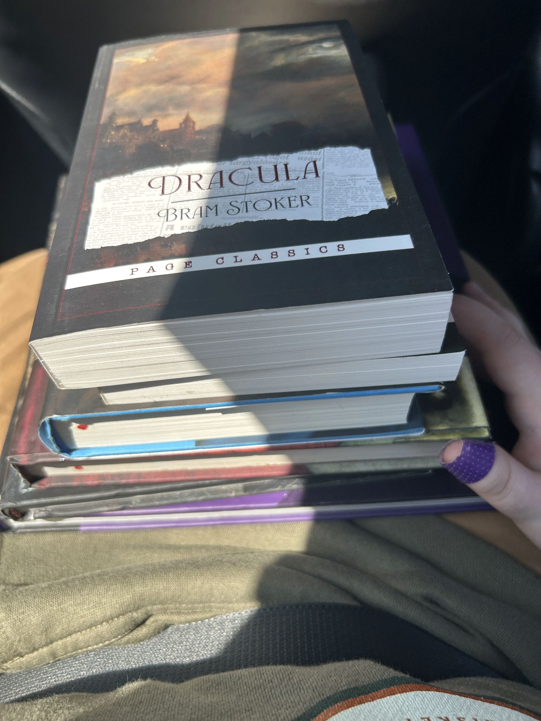 Image of five books stacked on someone's lap. Dracula by Bram Stoker is on top of the pile.